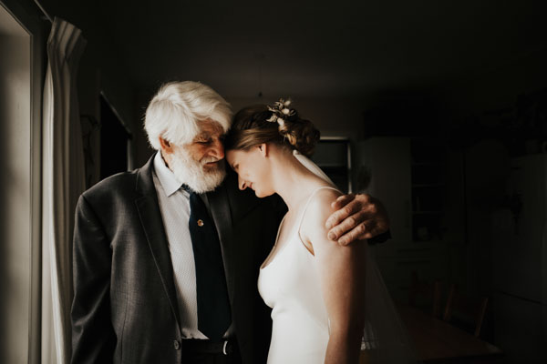 Bride sharing a quiet embrace with an older family member indoors.